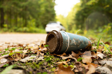 Old disposable coffee cup in the forest next to the road with car in a background. Plastic...