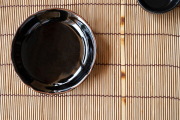 Am empty black ceramic plate with dark brown rim on a Japanese style bamboo mat.