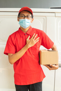 Asian Young Man Delivery In Red Uniform With Packages And Greet Hands On Chest