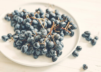 Black grapes in white plate staying in front light at wooden white table