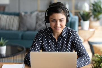 Attractive 25s indian woman sit at homeoffice room wearing headset take part in educational webinar...