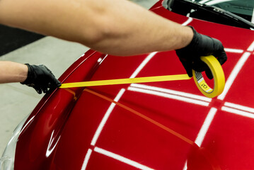 Car service worker applying protective tape on the car details before polishing.