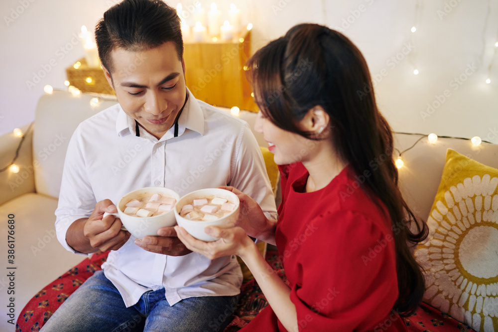 Poster Smiling young Asian boyfriend and girlfriend drinking hot cocoa with marshmallows