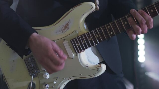 Man in a suit plays six-string electric guitar at concert. Close-up footage of musiian's hands at party with strobe disco lights.