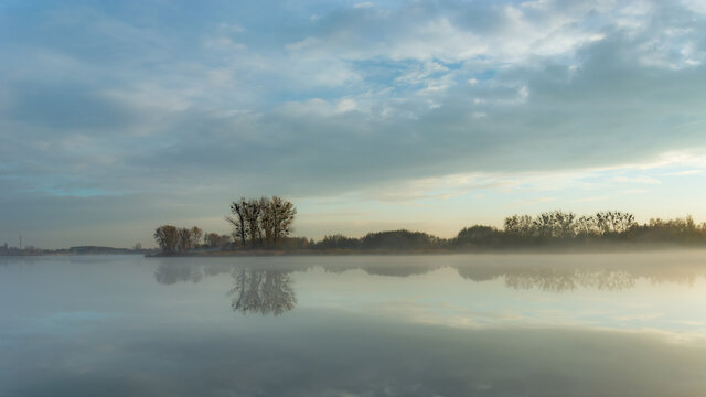 Fog over a calm lake, trees on the horizon © darekb22