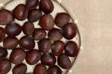 Chestnuts in bamboo basket isolated on jute background. Close-up. Copy space. Top view.