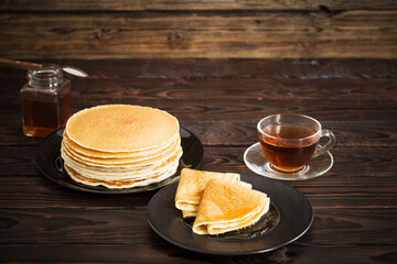 puncakes with honey and cup of tea on old wooden background