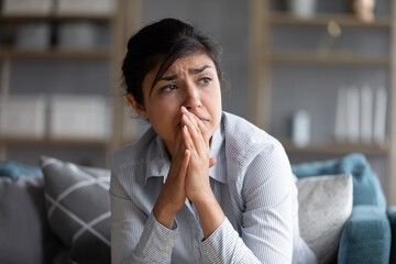 Sad indian woman feels miserable desperate sit on sofa look out the window thinking about personal troubles does not see way out of difficult life situation. Break up, heartbreak, cheated girl concept