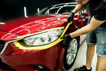 Car service worker applying protective tape on the car details before polishing.