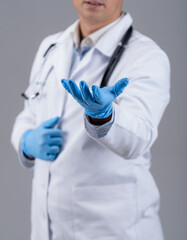 Doctor is showing one hand in blue medical gloves to the camera. Medic in white scrubs with phonendoscope. Cropped photo. Closeup.