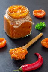 Traditional homemade spicy dried apricot chutney in glass jar on black background. Delicious sweet spicy sauce preserved for autumn and winter season. Vertical