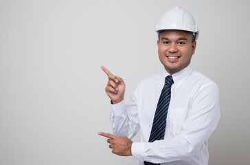 Asian worker in uniform hard hat pointing the finger to blank space for advertise text or mockup in studio isolated white background.