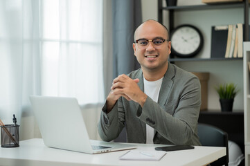 A middle-aged man around the age of 35. Working at home Work through the laptop by meeting video conference. He was wearing a grey suit and glasses. Smiling asian businessman work from home.