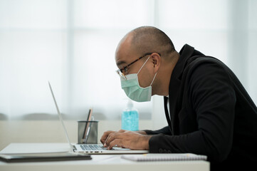 Fototapeta na wymiar Young businessman wearing protection mask working with laptop in office. Social distancing safety from corona virus flu.