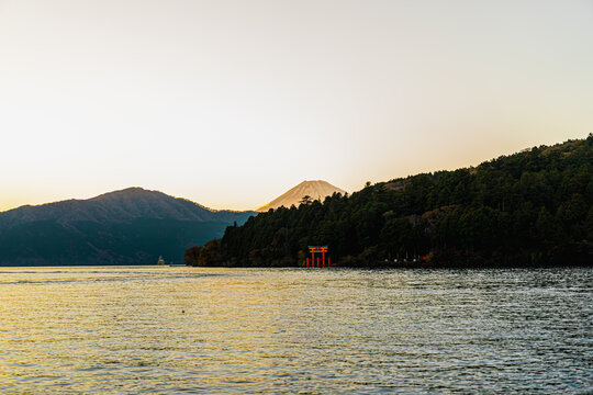 Front view of the lake with golden light and clear sky in soft tone. Mount Fuji with snow covering top of the volcano peak and Heiwa no Torii at Hakone, Japan. There are many trees with copy space.