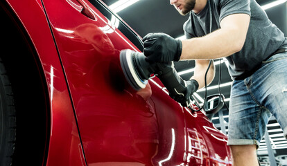 Car service worker polishes a car details with orbital polisher.