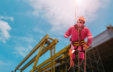 Worker Abseiling from high places Closeup pic of male rope access jobs worker wearing white hard hat, long sleeve shirt, safety harness, working at height abseiling down from the high rise.