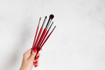 Professional makeup brush set in female hand with red nail design. beauty products, female face care accessory. white background with place for your text or design.