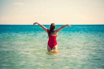 A young slender, beautiful European middle-aged woman is swimming in the sea, a mature brunette in a red bathing suit is enjoying her summer vacation. Freedom and cheerfulness concept
