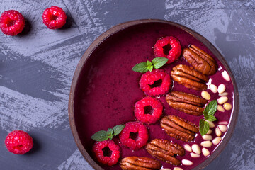 Smoothie bowl with raspberry, pecan, pine nuts and mint in a wooden bowl on the grey table. Top view