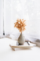 A vase of brown flowers placed on a book by the window.
