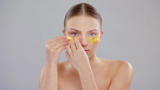 Close Up Beautiful Young Caucasian Blonde Woman With Blue Eyes And Smooth Healthy Skin Applying Under Eye Gold Patches Skin Care Cosmetic Concept Slow Motion On Grey Background