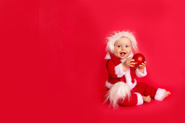 happy little baby six months old in Santa costume sitting on red isolated photophone with Christmas balls, space for text, new year and holiday concept
