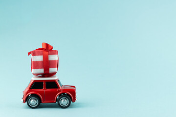 Red toy model car with gift box on blue background. Christmas and New year delivery concept
