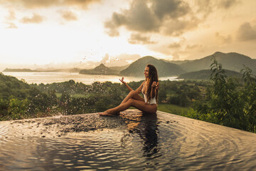 Dream journey in Asia. Woman sitting on edge luxury infinity pool an enjoying amazing mountain,...