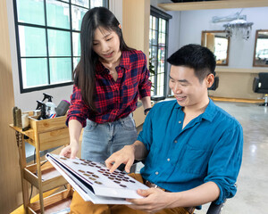 Obraz premium Hairdresser service customer in salon. Young Asian woman suggest hairstyle and color by using color palette to Asian Man in barbershop. Haircut and hair coloring concept.