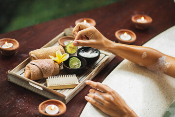Beauty spa treatment concept. Woman hands hold lime from natural cosmetics set on wooden tray. Romantic mood, candles around.