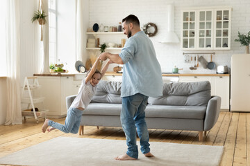 Happy young father spinning little daughter, holding hands, family playing funny active game at...
