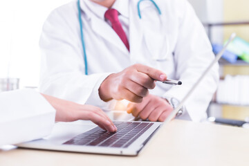 Unrecognizable doctor working with team on laptop computer in doctor’s office. Professional...