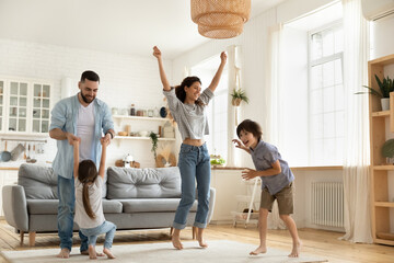 Happy parents with kids dancing in modern living room, having fun, playing active game, overjoyed...