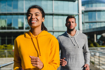 Smiling fit Afro girl in the foreground jogging with handsome caucasian male runner in urban area