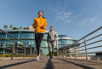Fototapeta na wymiar Full length portrait of two mixed race female and male runners jogging against glass skyscraper