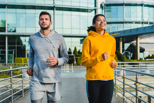 Young Sporty Mixed Race Couple Running Together Against Modern Building Made Of Glass