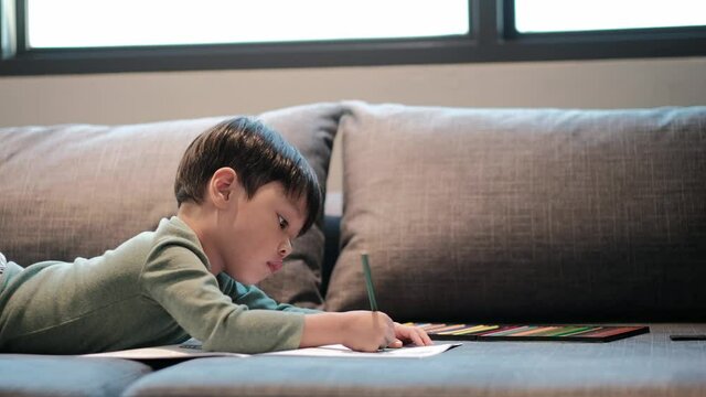 Little asian boy having fun on sofa, boy was coloring cartoons on coloring book at home. Coloring Book Education Talent Concept. Copy space.