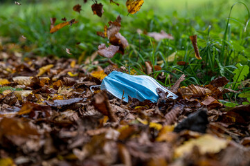 Protective mask lying on autumnal leaves. More leaves are falling down.