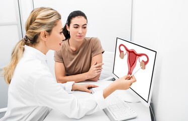 Gynecologist consulting a woman patient, talking about diseases of the uterus and ovaries, pointing...