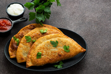 Homemade chebureks with filling and tomato sauce on a dark background