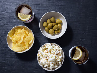Popcorn, olives, chips and beverages on a textured blue table. Top view