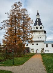 Naklejka premium Ancient Russian monastery with golden domes and white bright walls with yellow autumn trees in the foreground. Landscape