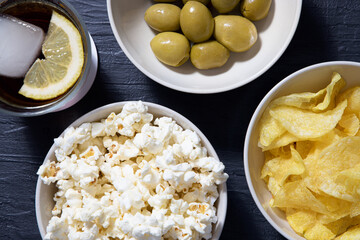 Popcorn, olives, chips and beverages on a textured blue table. Perspective