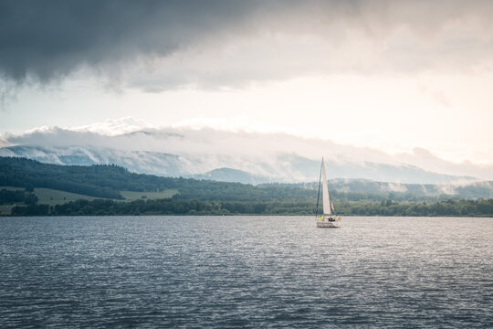 Sailing boat floats on the lake with stormy clouds sky. Autumn sailboat ship water sport scene from Lipno, Czech republic, Sumava.