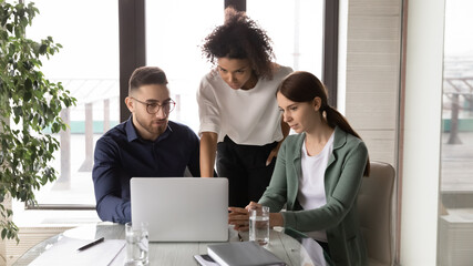 Young arab male manager discussing online project on computer with multiracial female colleagues, brainstorming together at office meeting. Mixed race business people busy with problem solution.