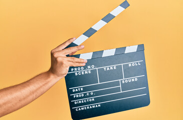 Hand of hispanic man holding movie clapboard over isolated yellow background.