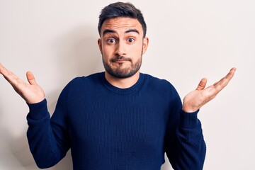 Young handsome man with beard wearing casual sweater standing over white background clueless and...
