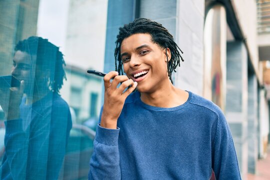 Young african american man sending audio message using smartphone at street of city.