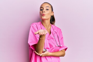 Young hispanic woman wearing doctor uniform and stethoscope looking at the camera blowing a kiss...